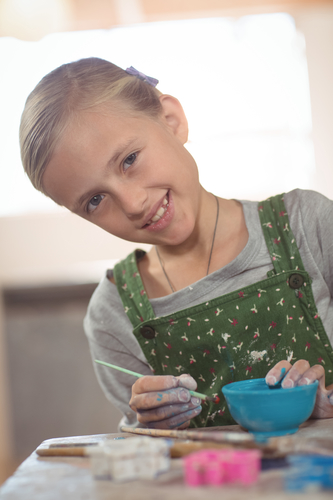 Portrait of smiling girl painting on bowl in pottery workshop